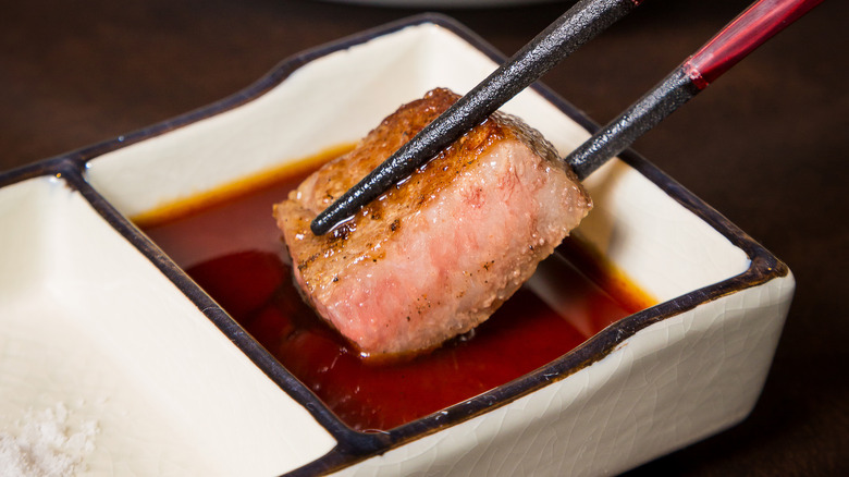 Piece of Wagyu steak being dipped into soy sauce using chopsticks