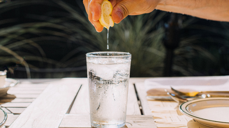 Wedge of lem0on being squeezed into a glass of sparkling water outside