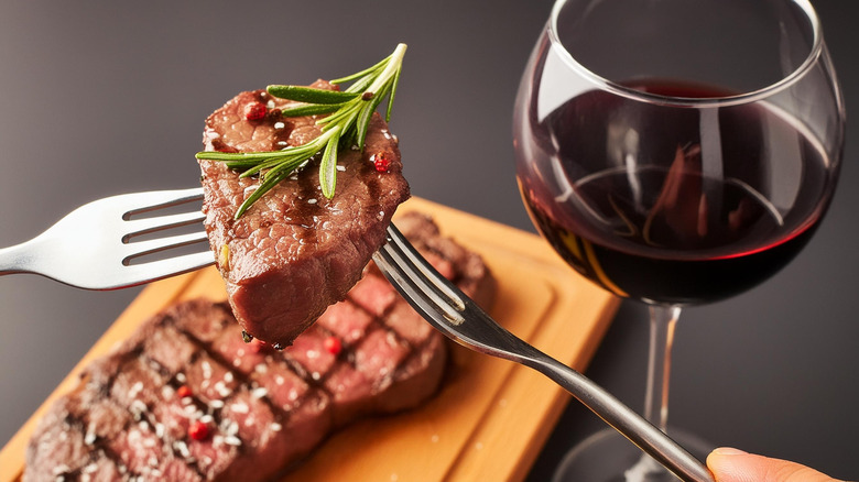 Forkful of grilled steak being lifted up with glass of red wine