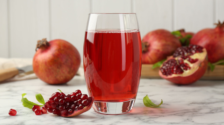 Glass of pomegranate juice surrounded by the fruit and loose arils