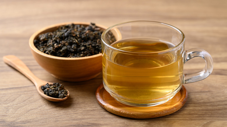 Oolong tea in a glass cup with wooden bowl of tea leaves