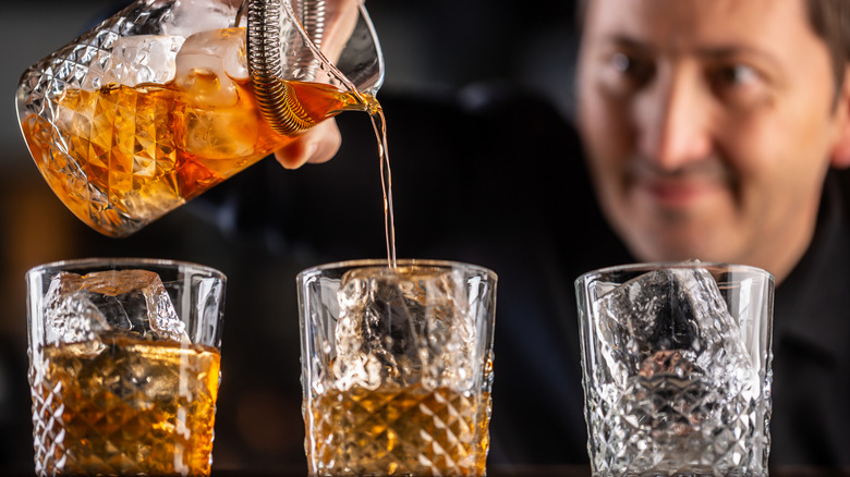 person pours old fashioneds into glasses