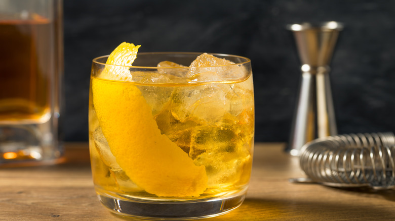 Rusty Nail cocktail with orange garnish on wooden table