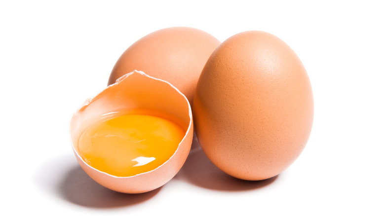 Three eggs, one cracked open to reveal the yolk, sit against a white background