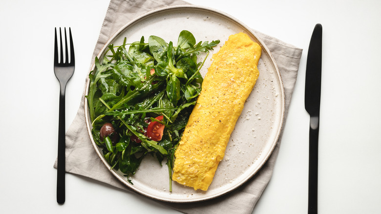 A French omelet sits on a white plate with an arugula salad