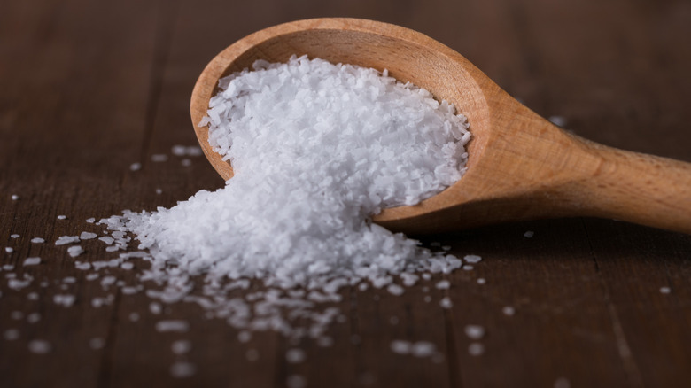 Salt pours from a small wooden spoon, onto the table