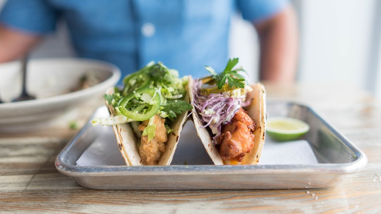 Fried seafood tacos topped with cabbage, cilantro, and sliced jalapeño on a metal platter