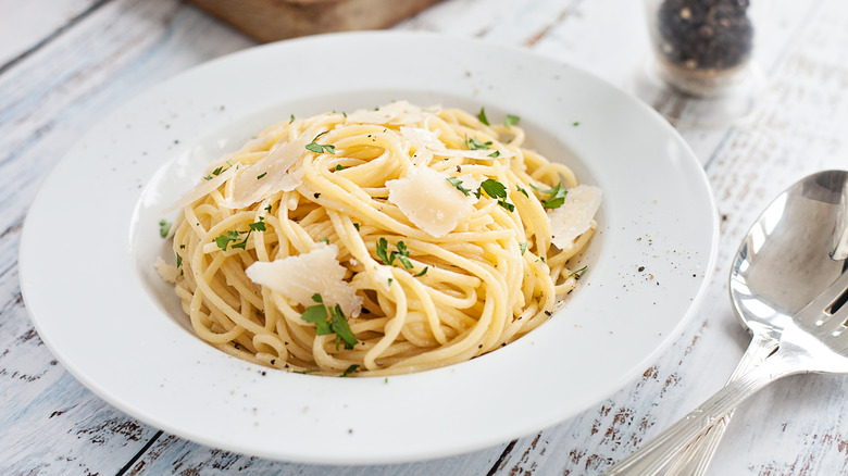 Bowl of pasta with herbs, butter, and cheese on a white wooden table