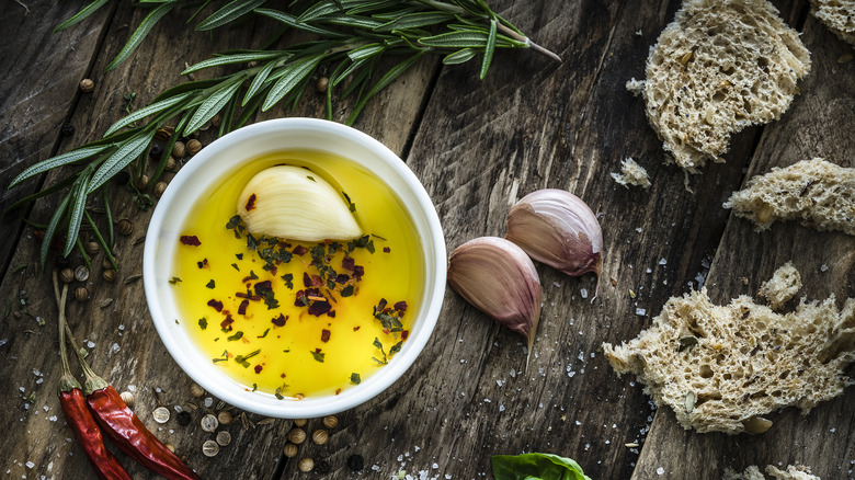 Olive oil with red pepper flakes, herbs, and garlic on wood.