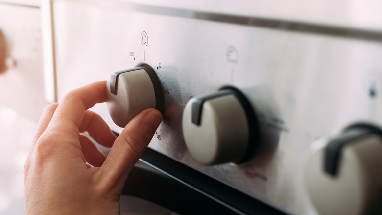 A hand turns a dial on the front of a stove