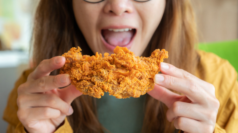 A girl about to bite down on a crispy fried piece of chicken