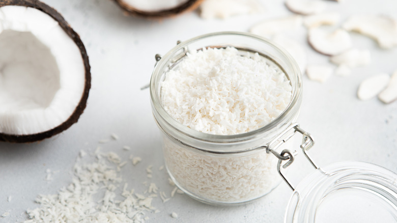 a glass jar of coconut flakes with ripe coconuts split open to the left