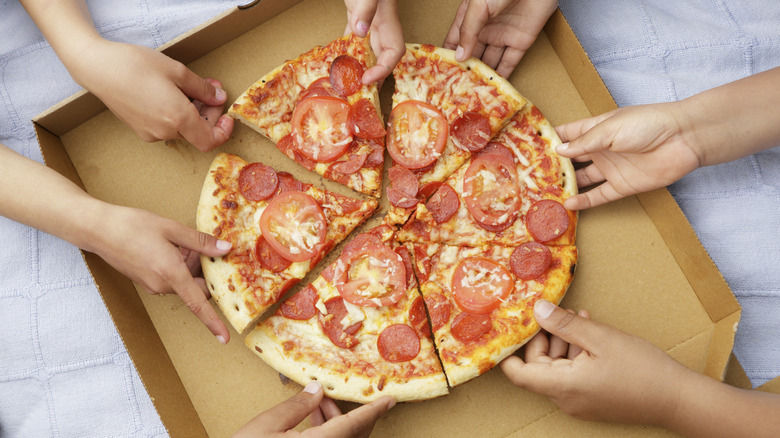 Hands grabbing slices of pepperoni and tomato pizza from box