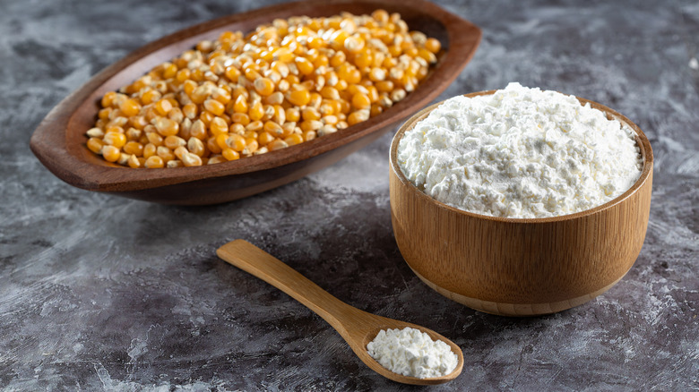 bowl of cornstarch sits next to a spoon and a bowl of dried corn kernels