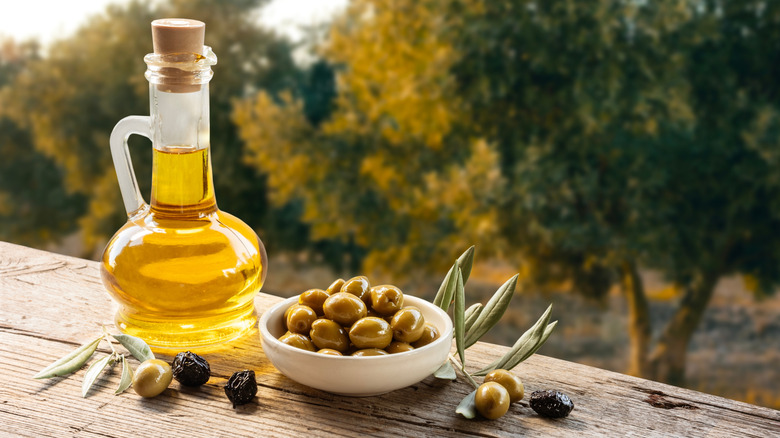 A jug of olive oil sits next to a bowl of olives