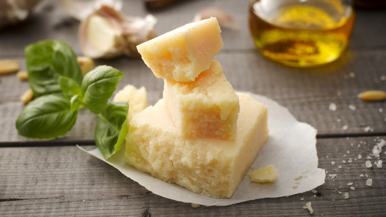 A small stack of rustic pieces of parmesan sit next to fresh basil, garlic, and a jug of olive oil