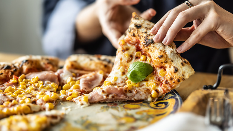 elote pizza on a table being picked up