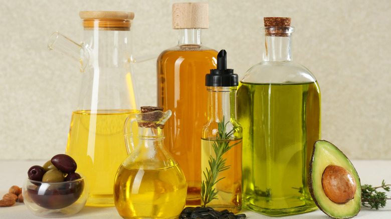 Different cooking oils next to herbs, avocados, and olives