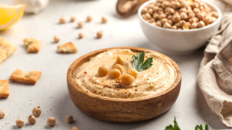 Hummus in a wooden bowl with whole chickpeas in background