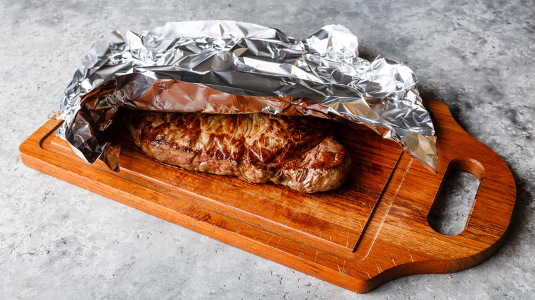 Steak tented with aluminum foil on a wooden board