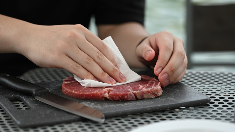 Chef pat drying a thin cut of steak on a cutting board