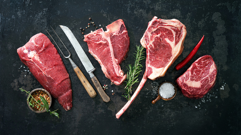 A variety of raw steaks with seasonings and cooking tools