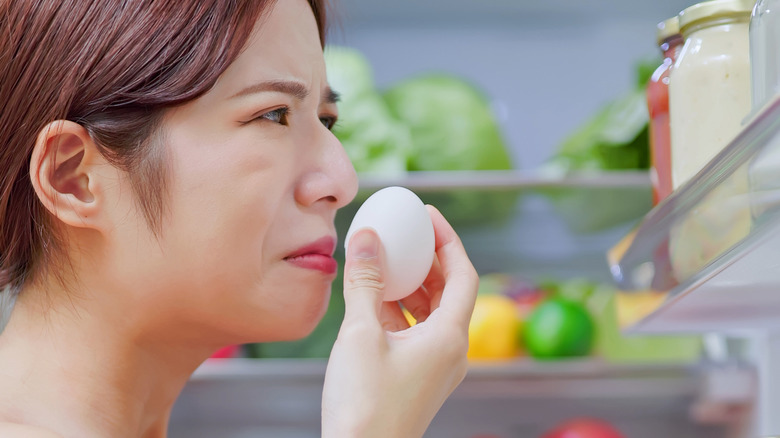 Woman smelling egg near fridge