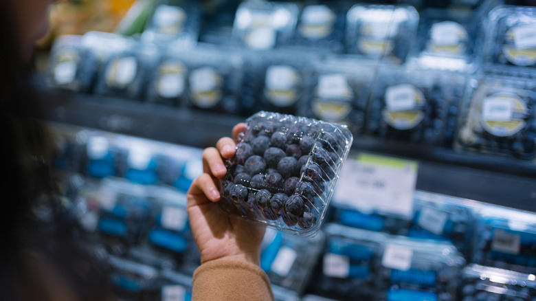 woman inspecting a clamshell container of blueberries