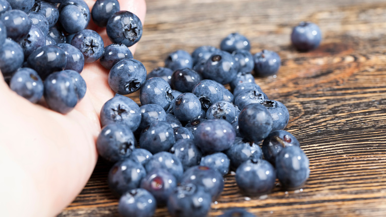 hand pouring fresh blueberries onto a wooden board