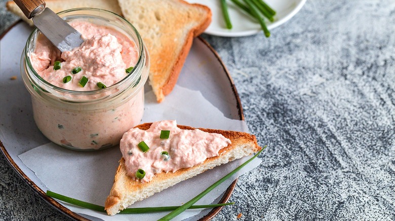 Creamy salmon dip in a small jar and on a small triangular piece of toast