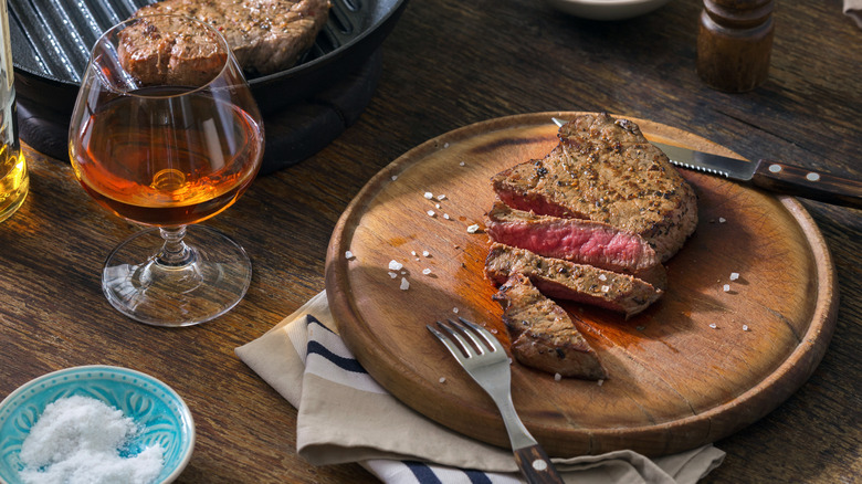Grilled steak on a wooden board with a glass of whiskey