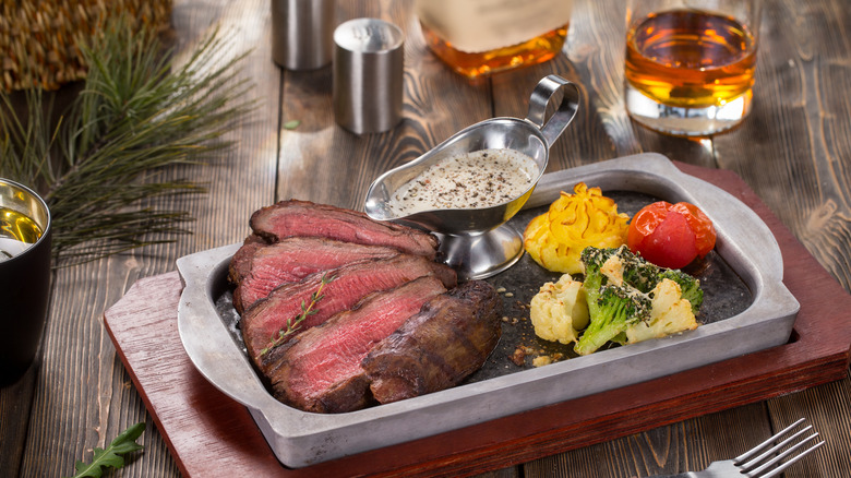 Grilled steak, steak sauce, and vegetables in a dish with a glass and bottle of whiskey