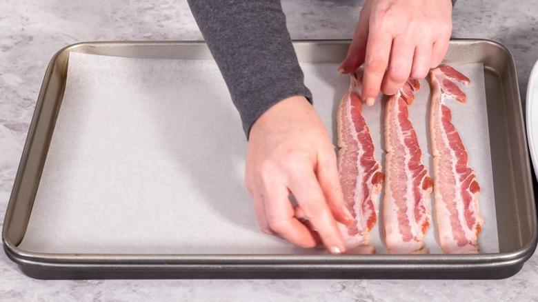 Laying strips of raw bacon on parchment lined sheet