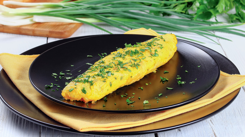 rolled omelet on black plate with greens