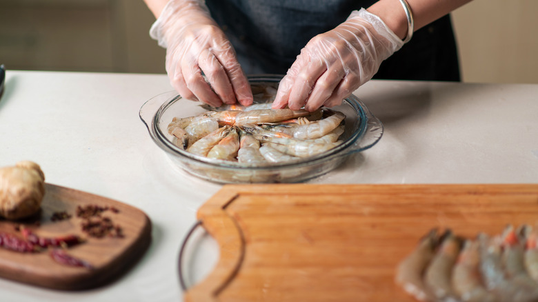 Rubber glove clad hands peeling shrimp in a kitchen