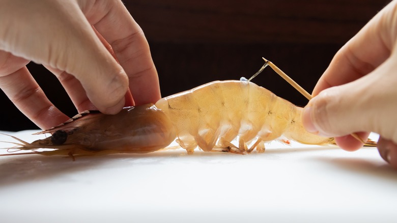 Hands removing vein from fresh shrimp with tooth pick