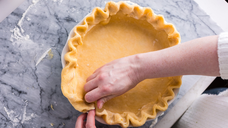 Someone crimping a pie crust before pouring in the pie filling.