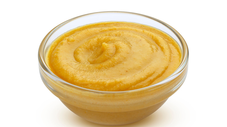 Glass bowl of mustard on white background