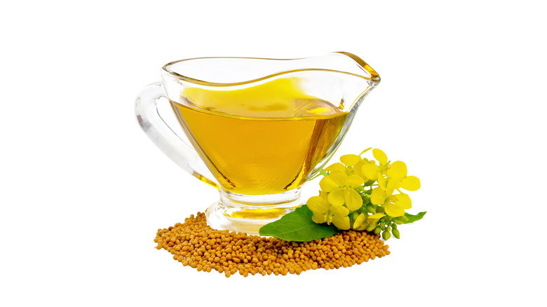 Mustard oil in pitcher with mustard seeds and flowers