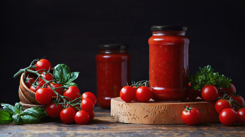 Jar of tomato sauce alongside fresh on the vine tomatoes