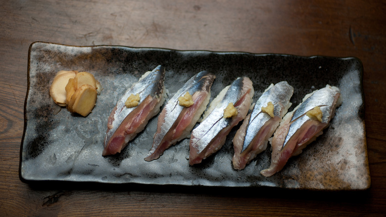 sanma sushi and sliced ginger on a platter on dark wooden table