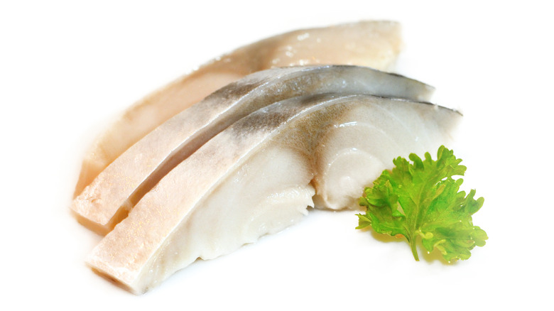 Mackerel sliced thinly with skin on alongside green garnish 