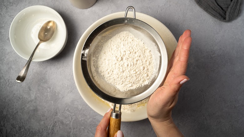 hands sifting flour through sieve 