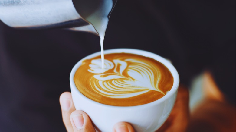 Pouring frothed milk into a mug of coffee