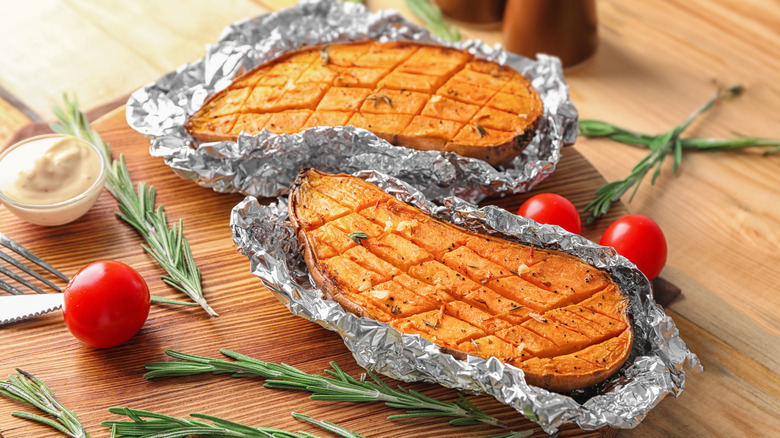 Sweet potato halves wrapped in foil on cutting board