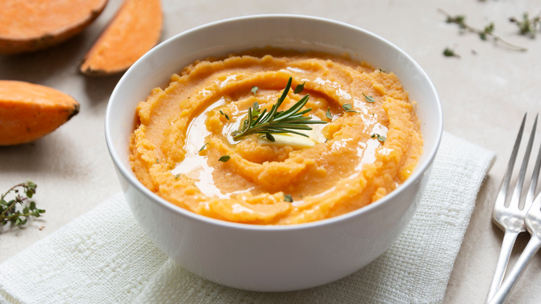 Mashed sweet potatoes in white bowl topped with butter and rosemary