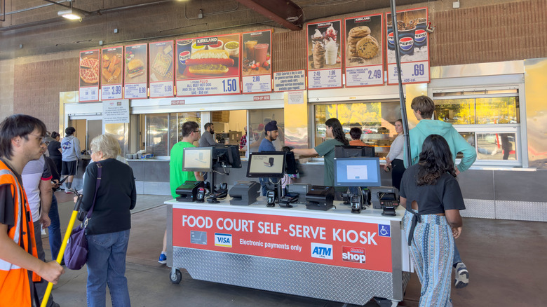 People mill around a Costco food court self-serve kiosk in front of the counter