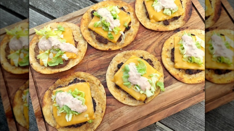 Smash burger tacos are lined up on a wooden cutting board.