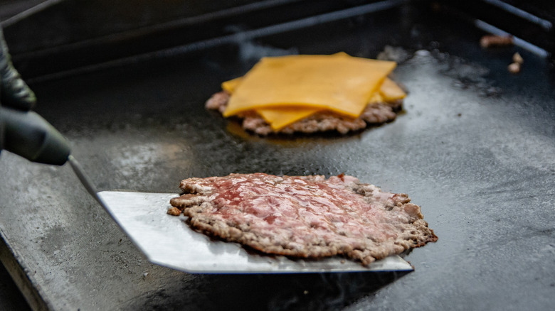 Smash burgers are being cooked on an outdoor flat-top griddle.