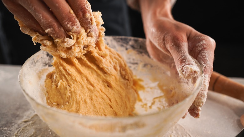 baker hand-mixing dough in bowl